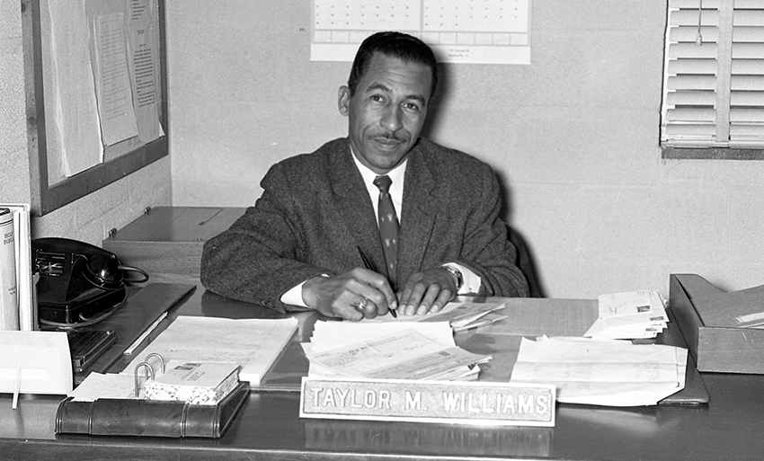 Black and white photograph of Principal Williams seated at his desk.